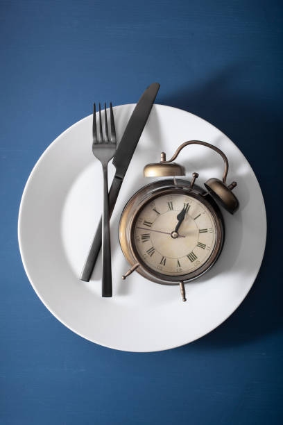 concept of intermittent fasting, ketogenic diet, weight loss. alarmclock fork and knife on a plate stock photo