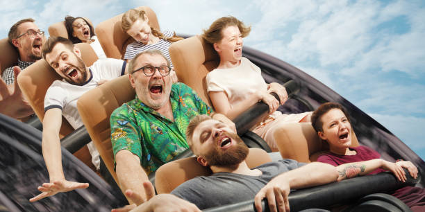 Moment of life, craziest things. Emotional people on the roller coaster going down wih meadows on background. Caucasian men and women get adrenaline activity and having fun together on the rides.