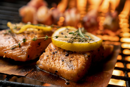 Beautiful sockeye salmon filet on a fiery grill with lemon slices and butter and bacon-wrapped shrimp, part of a ketogenic or low carb diet.