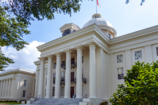 Montgomery Alabama State Capitol building with columns, steps,  Dome, flag and Clock showing