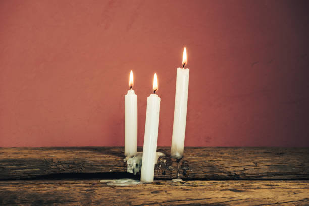 istock Beautiful three white burned candles on a old oak wooden table and red wall background. 1172241290