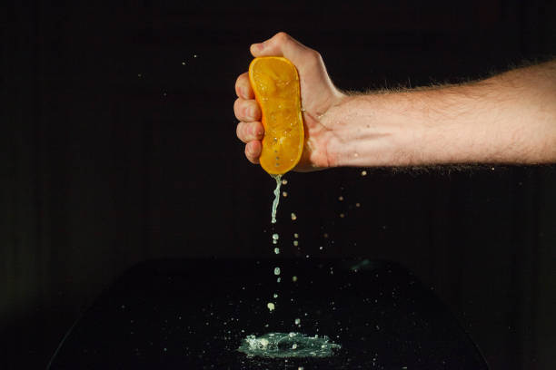 istock Strong man's hand squeezes half of an orange on glass table 1172244206