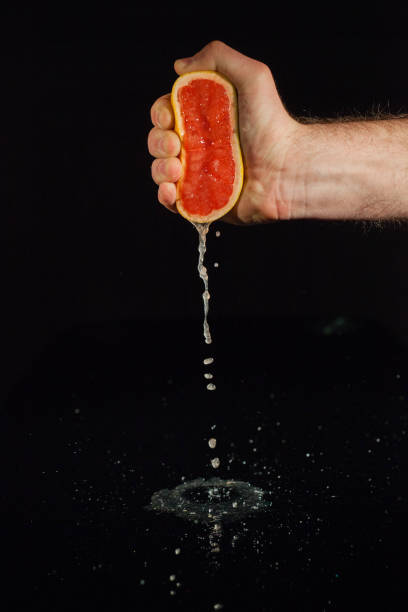 Grapefruit juice splashes from half of fruit held in man's hand