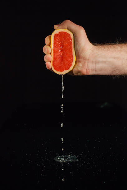istock Drops of grapefruit juice fall from fruit on black background 1172244413