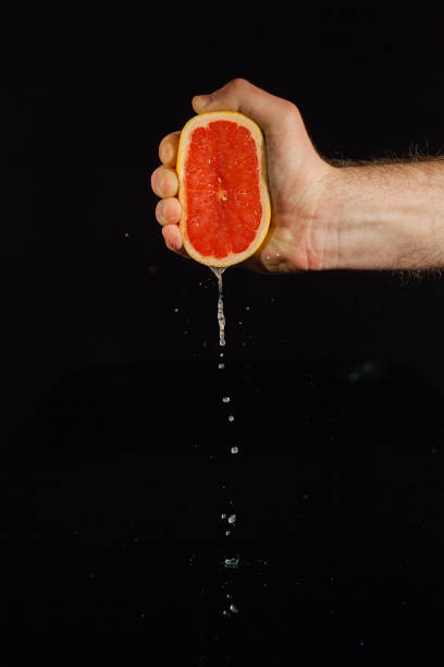 istock Drops of grapefruit juice fall from fruit on black background 1172244448