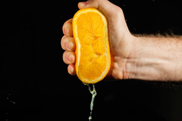 istock Juicy half of an orange held in stron man's hand 1172244491