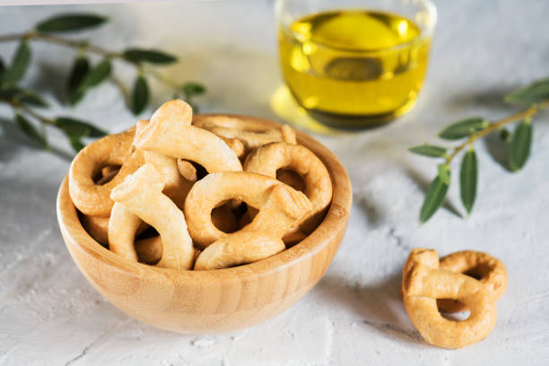 Taralli or tarallini is traditional Italian snack food typical of Apulia regional cuisine, copy space Taralli is a traditional Italian snack food typical of Puglia regional cuisine. Tarallini is in wooden bowl with olive twig. Ingredients: wine, olive oil, salt, flour of wheat grain and cereal products stock pictures, royalty-free photos & images