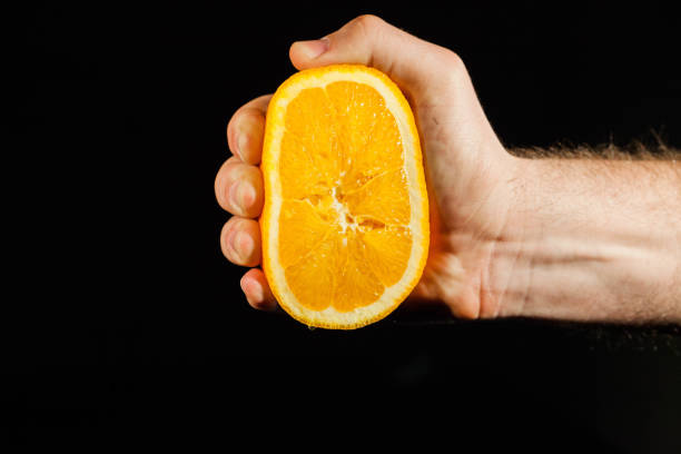Juicy half of an orange held in stron man's hand