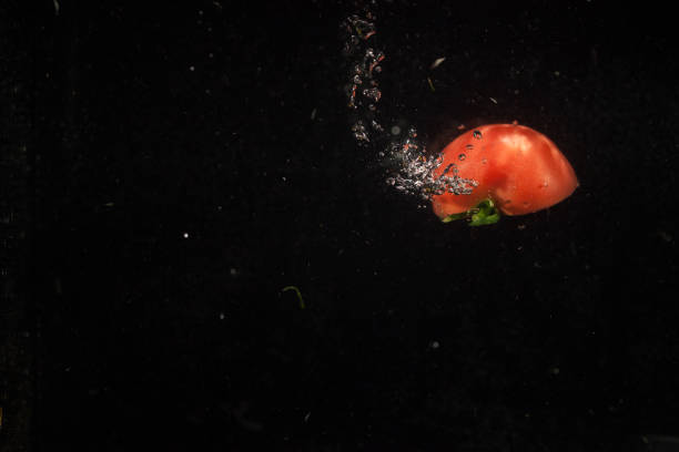 Half of juicy tomato splashes water falling on the bottom of black aquarium