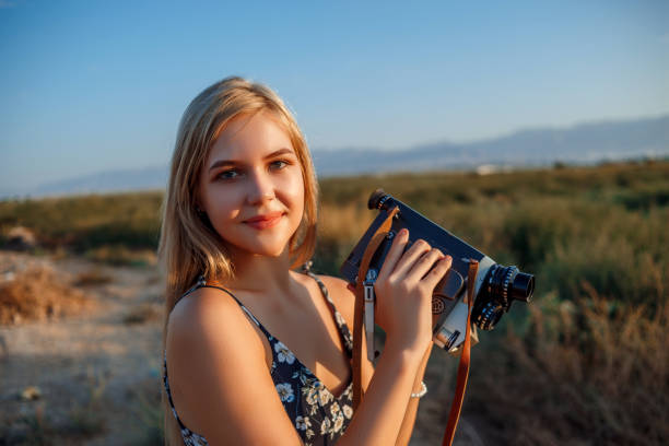 portrait of blonde girl in floral print dress with vintage video camera in grape field during sunset - photographer enjoyment elegance old fashioned imagens e fotografias de stock