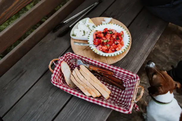 The man has an Italian style snack salad with mozzarella tomatoes and ciabatta bread outside on a wooden bench