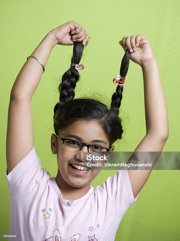 Один веселый индийская девочка держит ее plaits на зеленом фоне - Стоковые фото 10-11 лет роялти-фри