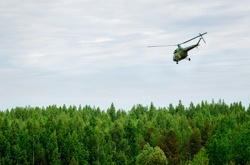 Khaki colored helicopter is flying in blue sky above forest
