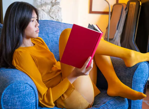 Asian young girl reading a book in blue armchair dress in yellow