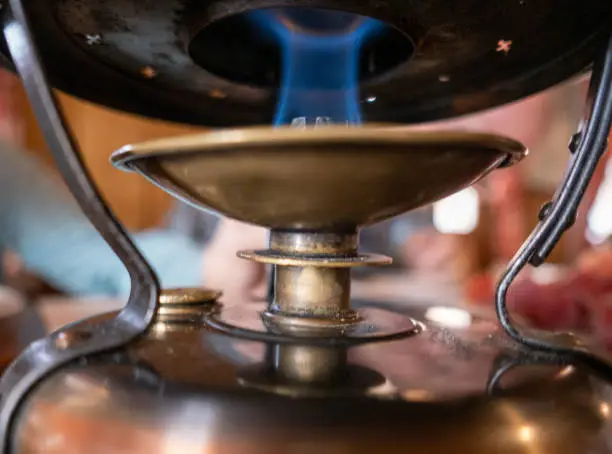Photo of Fondue burner burning below a cast iron cooking pot, at a restaurant table