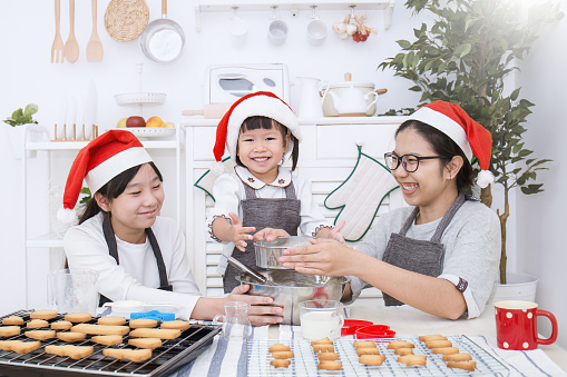 Little asian girl and her mother baking cake and cookies in the kitchen christmas eve holiday celebration. Happy asian family