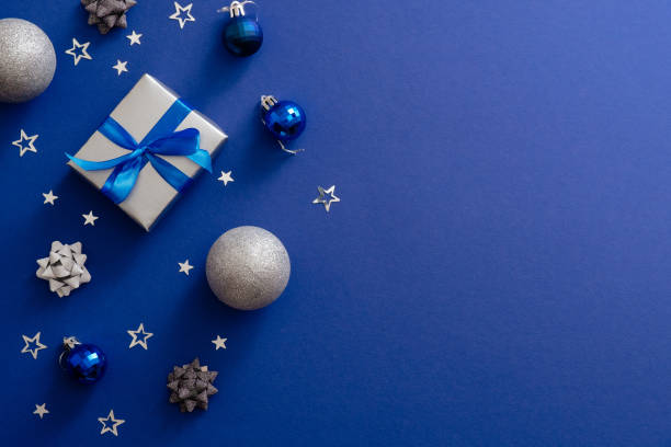 istock Christmas silver gift box with bow ribbon, baubles, decorations, confetti on magic dark blue background with copy space. Vintage Xmas greeting card mockup, postcard template. Flat lay, top view. 1172269677