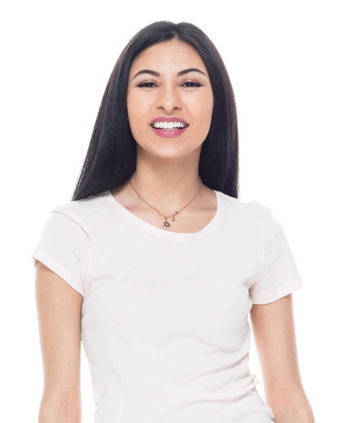 Front view / waist up of 20-29 years old adult beautiful / long hair latin american and hispanic ethnicity female / young women standing in front of white background wearing t-shirt / shirt who is smiling / happy / cheerful / cool attitude with hand by side vista frontal / cintura para arriba de 20-29 años de edad adulto hermoso / pelo largo latinoamericano y etnia hispana mujer / mujeres jóvenes de pie frente a fondo blanco usando camiseta / camisa que es sonriente / feliz / alegre / actitud fresca