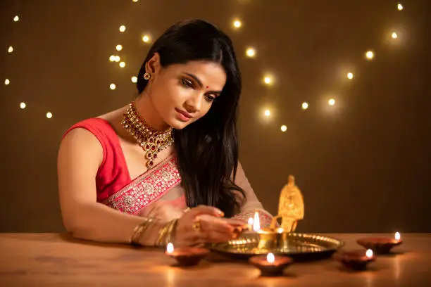 Beautiful Hindu Indian young women lightening Diya on Diwali day.