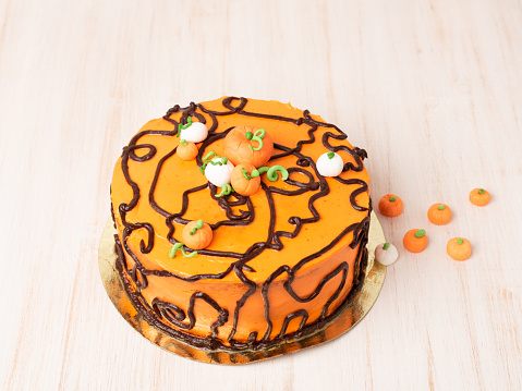 Pumpkin or carrot cake with cream cheese frosting decorated with candy, dessert for Halloween and Thanksgiving on wooden table