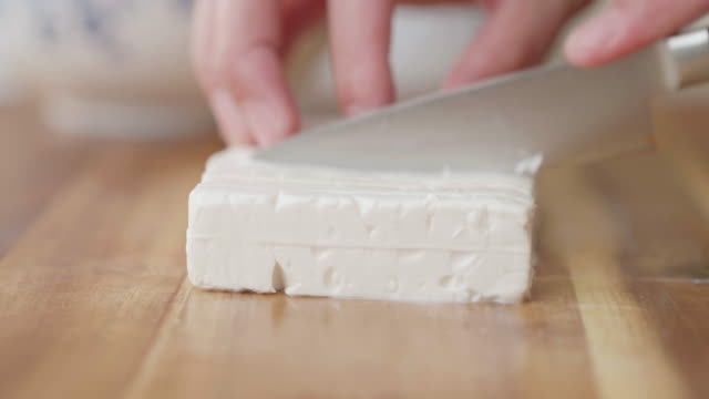 hand cut feta cheese into cubes on wooden chopping board