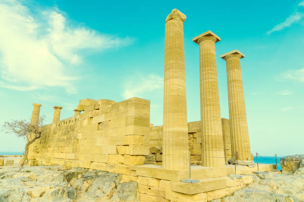 Doric temple of Athena Lindia on Acropolis of Lindos Rhodes, Greece. Front view of columns and walls. near tree grows. Doric temple of Athena Lindia on Acropolis of Lindos Rhodes, Greece. Front view of columns and walls. acropole stock pictures, royalty-free photos & images
