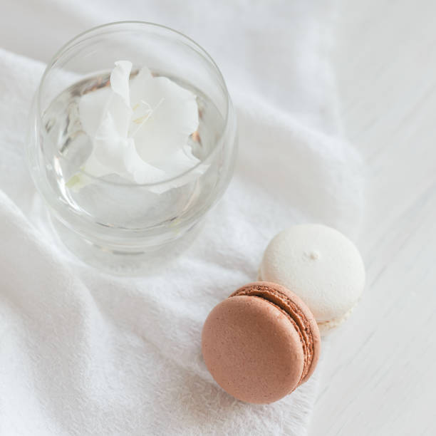 Two pastel French macarons  and glass with flower on a white background.