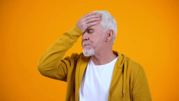istock Gray-haired pensioner showing face-palm gesture against orange background, fail 1172311235