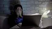 Young female watching scary movie, hiding face in fear, online film service