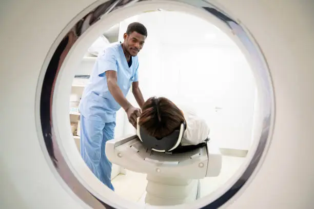 Photo of Friendly black male radiologist getting ready a patient for a CAT scan smiling