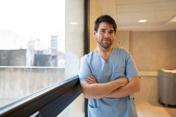 enfermera latinoamericana amigable apoyada en la ventana frente a la cámara con los brazos cruzados - nurse doctor healthcare and medicine latin american and hispanic ethnicity fotografías e imágenes de stock