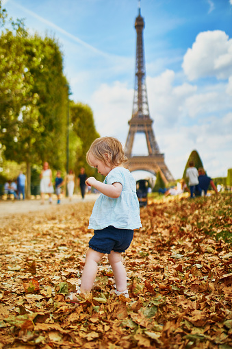 Adorable toddler girl walking on fallen autumn leaves near the Eiffel tower in Paris, France