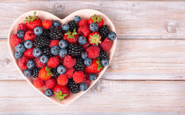 Assorted berries in a heart plate on white rustic wooden table