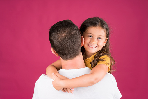Happy little girl hugs his dad, pink background