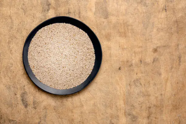 organic white chia seeds rich in omega-3 fatty acids,  top view of a black plate against textured bark paper