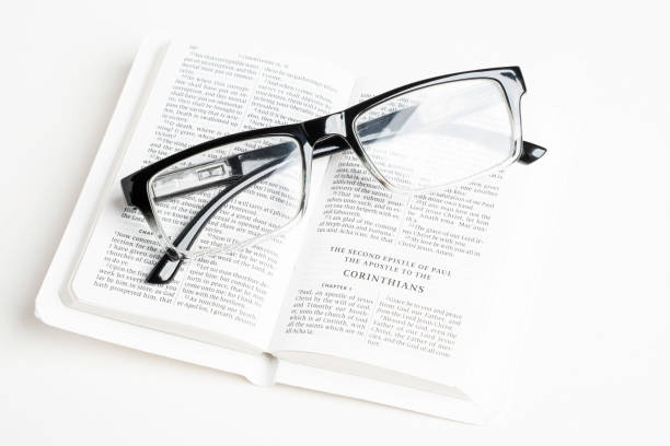 White Pocket Bible With A Pair Of Reading Glasses An open white portable pocket bible with a pair of clear reading glasses set on plain white background. read the fine print stock pictures, royalty-free photos & images