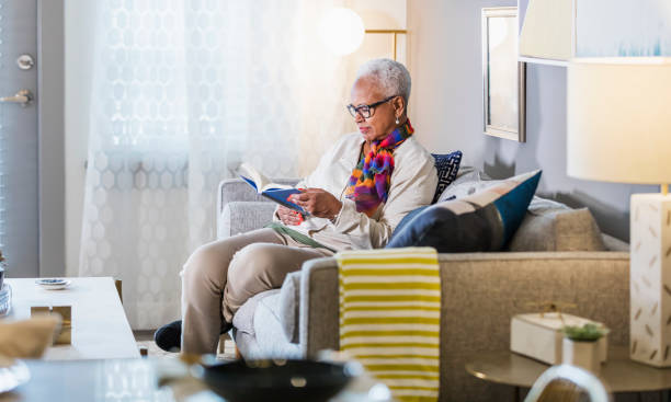 自宅で読書に座っているシニアアフリカ系アメリカ人女性 - senior adult relaxation sofa reading ストックフォトと画像