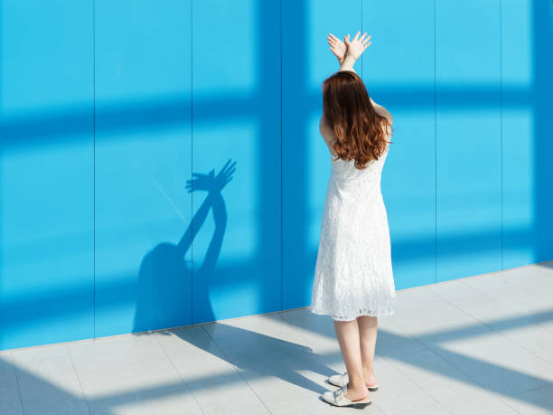 hermosa mujer morena china en vestido de novia blanco bailando con sus sombras sobre fondo de pared azul. soleado retrato de glamour joven dama elegante. emociones, belleza y concepto de estilo de vida. - boda coreana fotografías e imágenes de stock