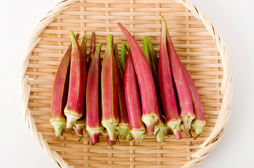 fresh Red okra on bamboo colander on white background