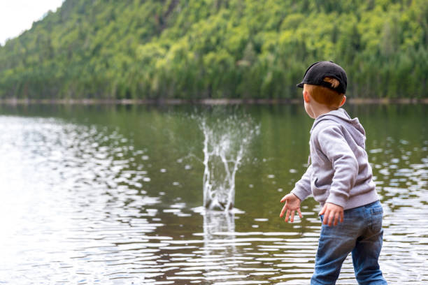 il piccolo ragazzo rossa che lancia pietre nel lago in estate - throwing people stone tossing foto e immagini stock