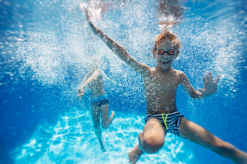 Smiling kids dancing underwater in the pool. Sunny summer day.
Nikon D850