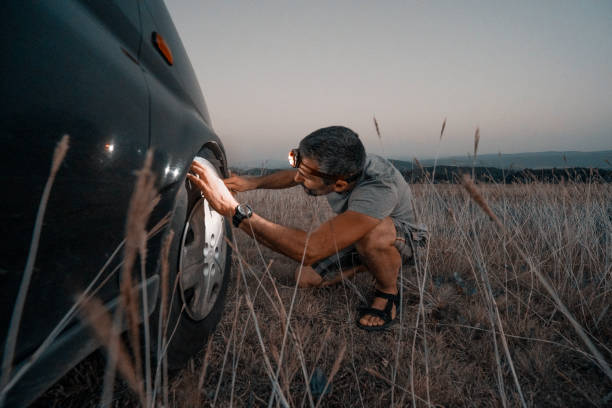 Car repair. Lucky me. Changing car tire in the middle of nowhere at dusk. DIY Sunday night adventures. A middle-aged handsome man changing his car tyre in a deserted place somewhere in the wild. Urgency measures. flat tire stock pictures, royalty-free photos & images