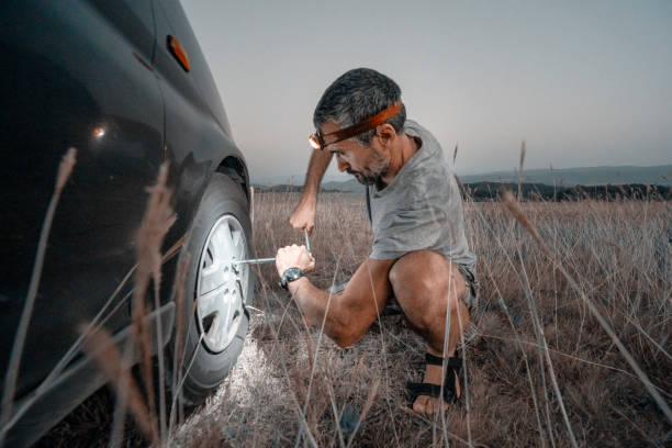 car repair. lucky me. changing car tire in the middle of nowhere at dusk. diy - roadside emergency imagens e fotografias de stock