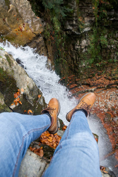 istock man legs in blue jeans and brown boots sitting on the edge looking at waterfall 1172410571