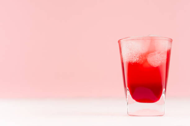 Tropical refreshment alcohol red shot drink with ice cubes on white wood board and pastel pink background, copy space. Tropical refreshment alcohol red shot drink with ice cubes on white wood board and pastel pink background, copy space. red drink stock pictures, royalty-free photos & images