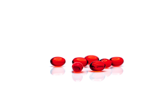 Red soft gel capsule pills isolated on white background. Pile of red soft gelatin capsule. Vitamins and dietary supplements concept. Pharmaceutical industry. Pharmacy drug store. Health care products.