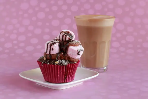A marshmallow cupcake on a white plate with coffee.