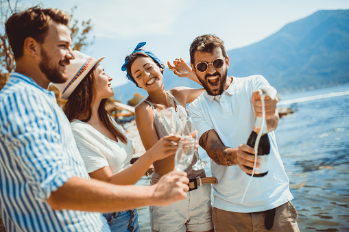 Young attractive and trendy people standing over the sea and drinking champagne while smiling broadly.