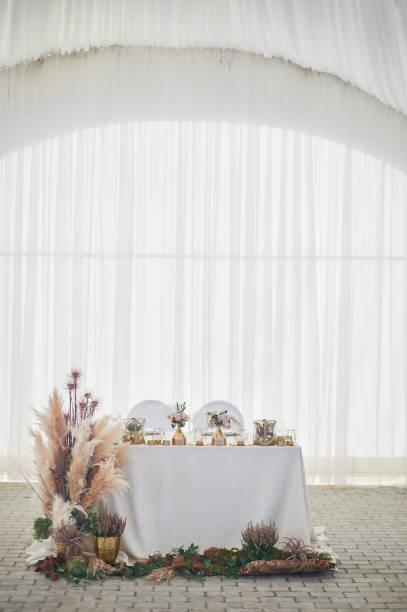 istock Wedding decoration in boho style.Light colors, in the tent.Wedding table decorated with pampas grass. Roses and gold geometric candlesticks 1172423206
