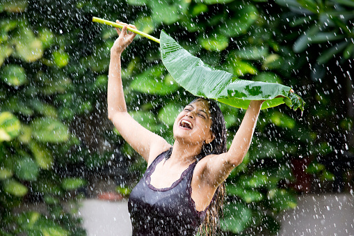 Excited woman holding banana leaf over her head enjoying rain